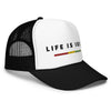 Black and white trucker hat featuring front 3D embroidered "life is irie" text and Reggae stripe in red, gold, green. Mesh back with adjustable closure.  